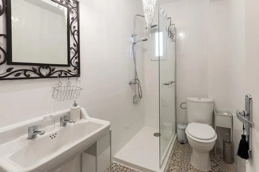 A bright bathroom with a sink, mirror, shower, and toilet.