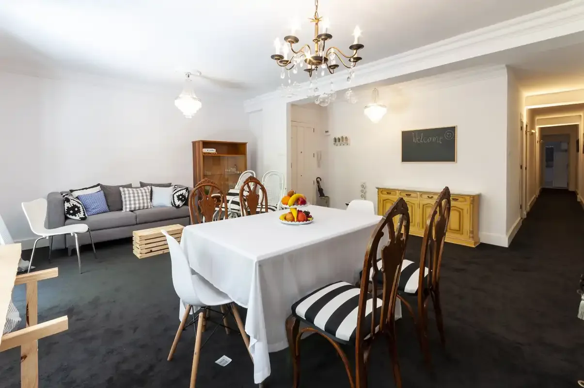 A dining area with a set table, seating, and a living room in the background.