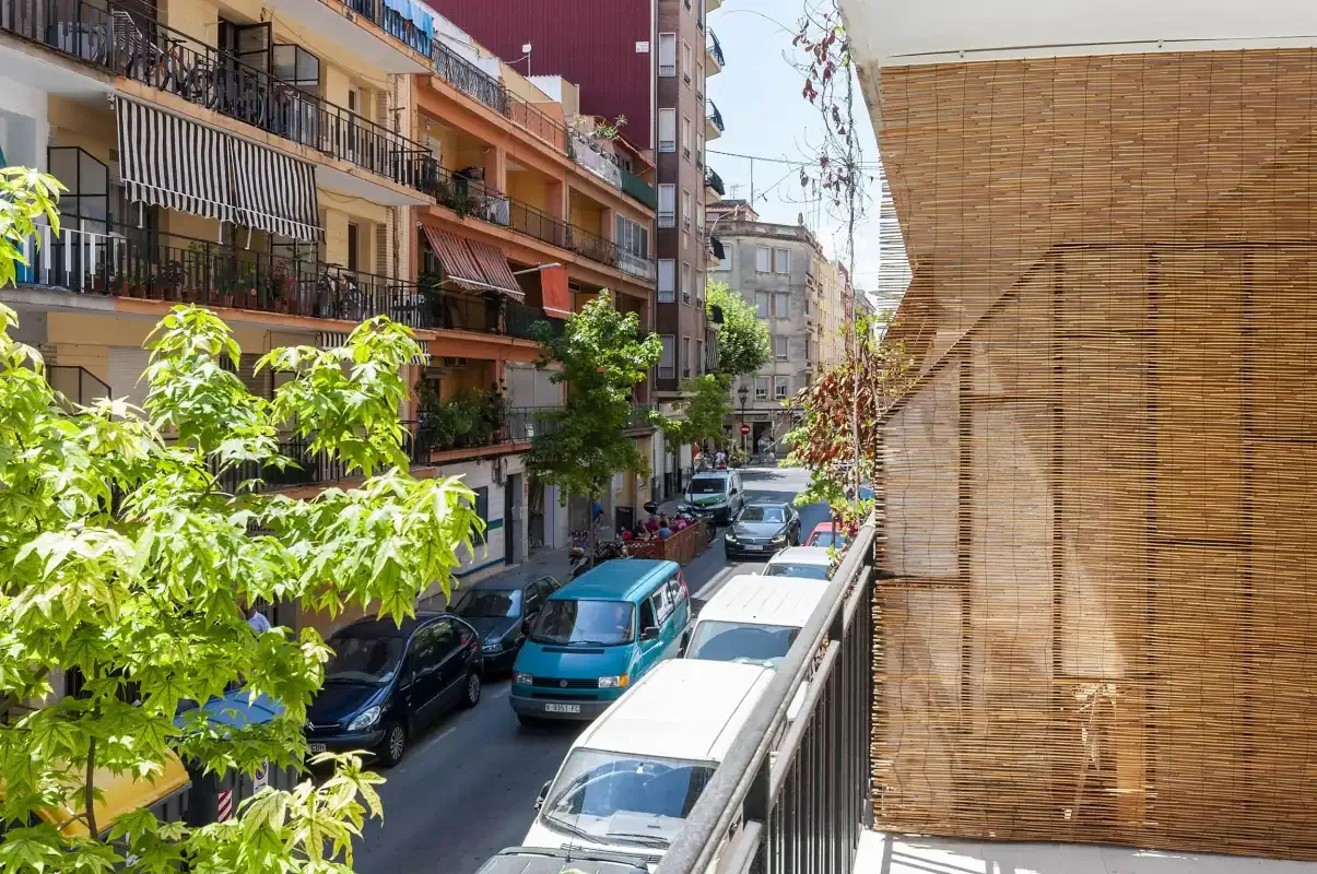 A balcony overlooks a residential street lined with parked cars and apartment buildings.