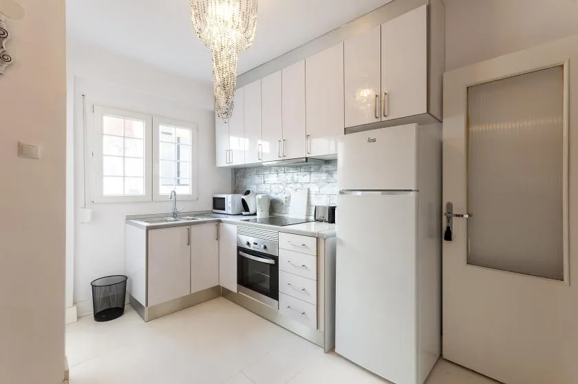 A bright kitchen with white cabinetry, a refrigerator, and a window.