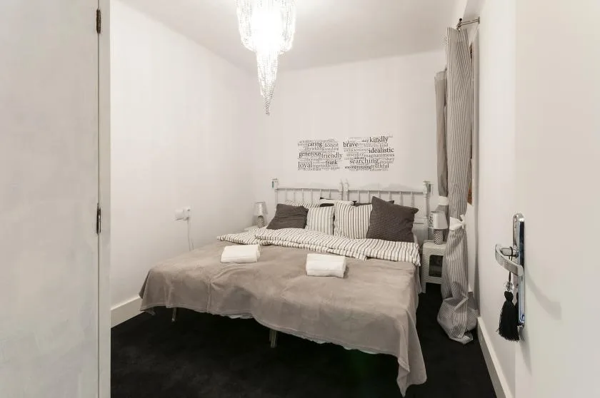A bedroom with a neatly made bed and a hanging chandelier.