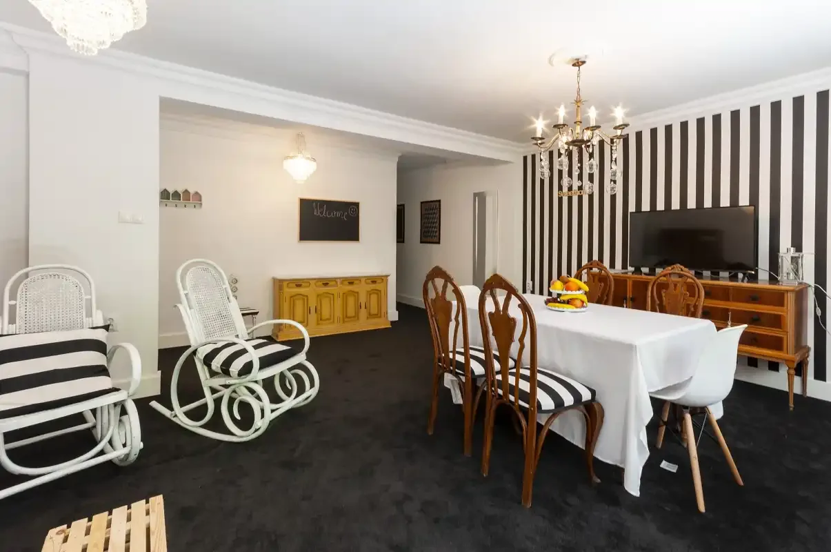 A dining area with a long table, seating, and a television against a striped wall.