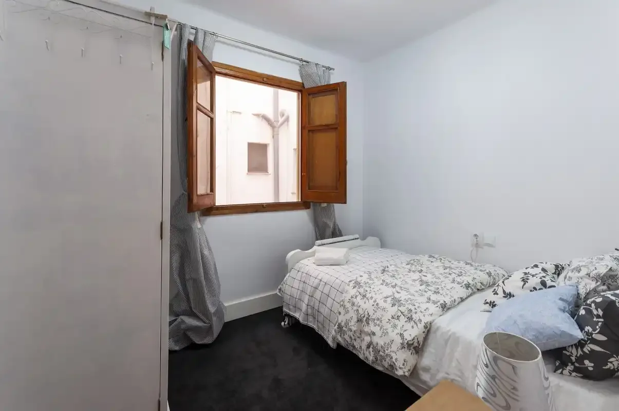 A bedroom with a bed beneath an open wooden window.
