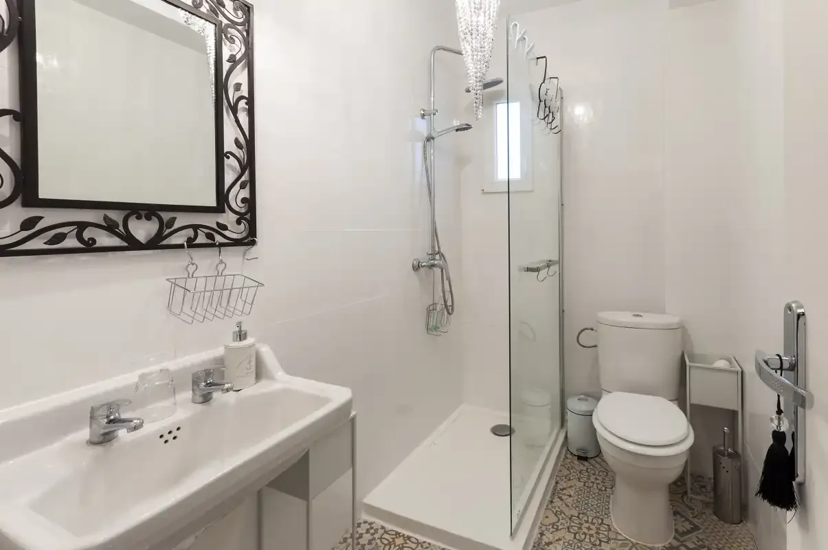 A bright bathroom with a sink, mirror, shower, and toilet.