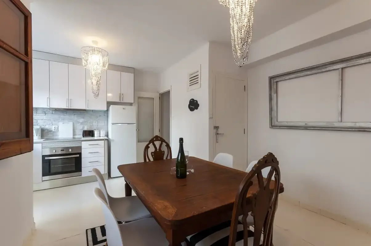 A dining area with a wooden table sits beside a compact kitchen.