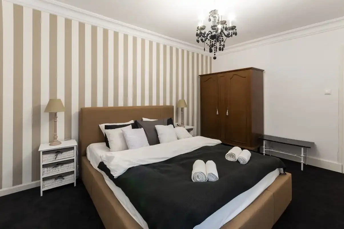 A bedroom with a bed, striped wallpaper, and a wooden wardrobe.