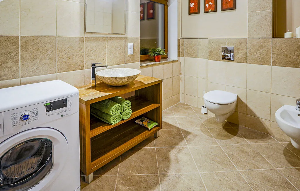 A tiled bathroom with a wooden vanity, wall-mounted toilet, and washing machine.