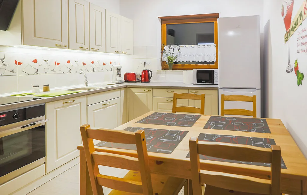 A bright kitchen with pale cabinets, a dining table, and wooden chairs.