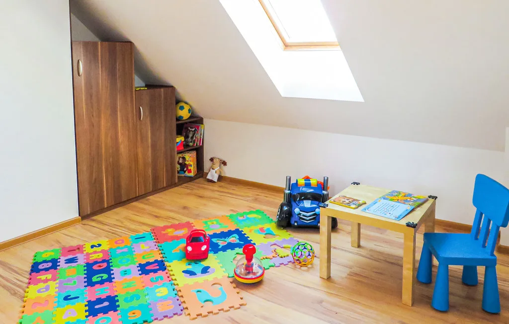 A playroom with colorful floor mats, toys, and a small table beneath a skylight.