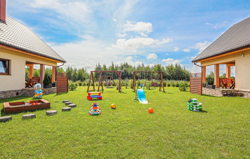 Una zona de juegos al aire libre con césped, columpios, un tobogán y juguetes.