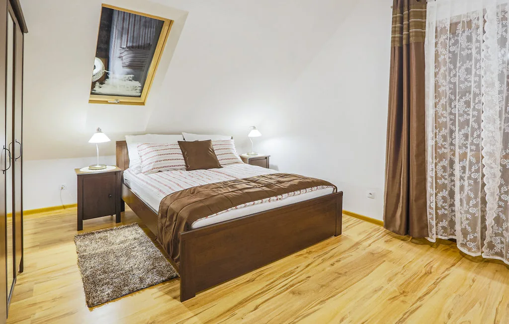 A bedroom with a made bed, bedside tables, and curtains beside a window.