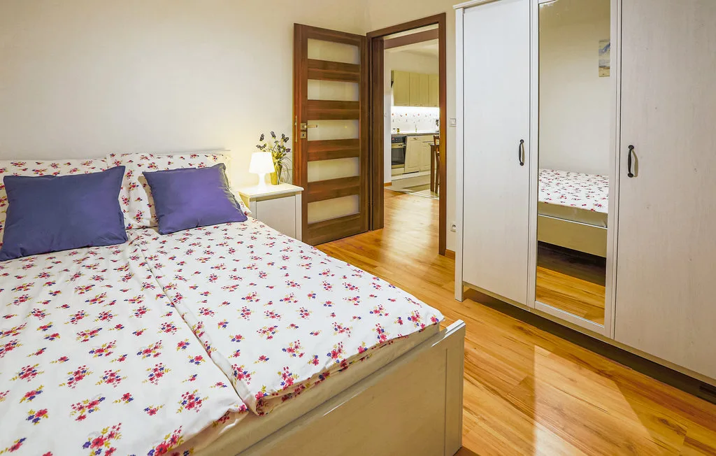 A bedroom with floral bedding, purple pillows, and a mirrored wardrobe.