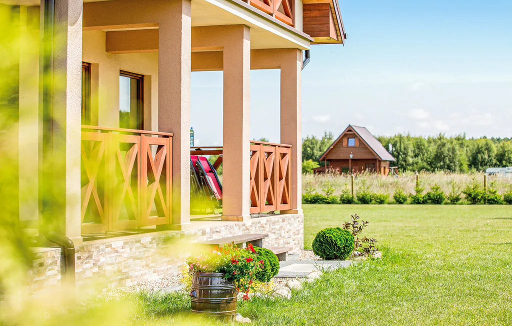 A house veranda overlooks a grassy yard with another house in the distance.