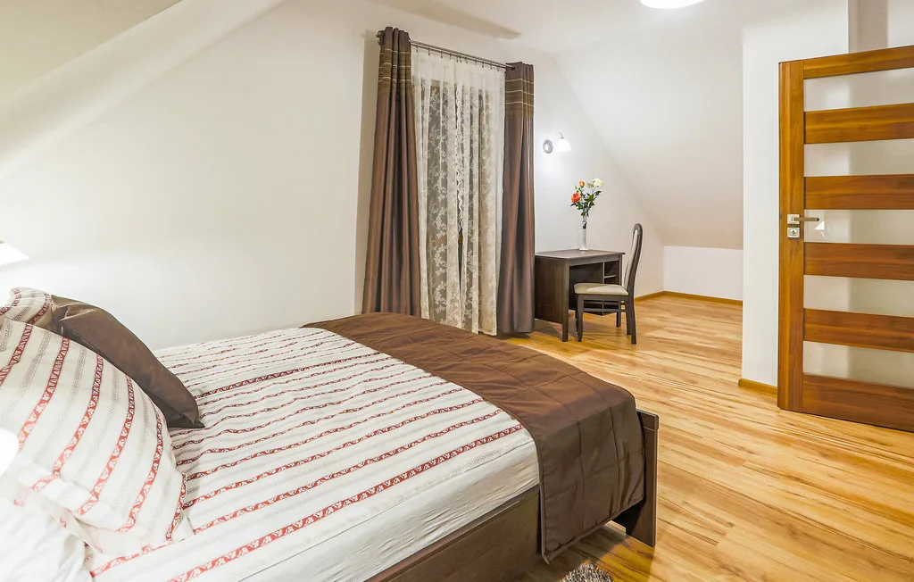 A bedroom with a bed, a small desk, and a wooden door.