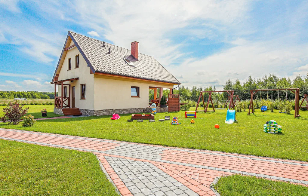 A house stands beside a grassy yard with outdoor play equipment and a paved path.