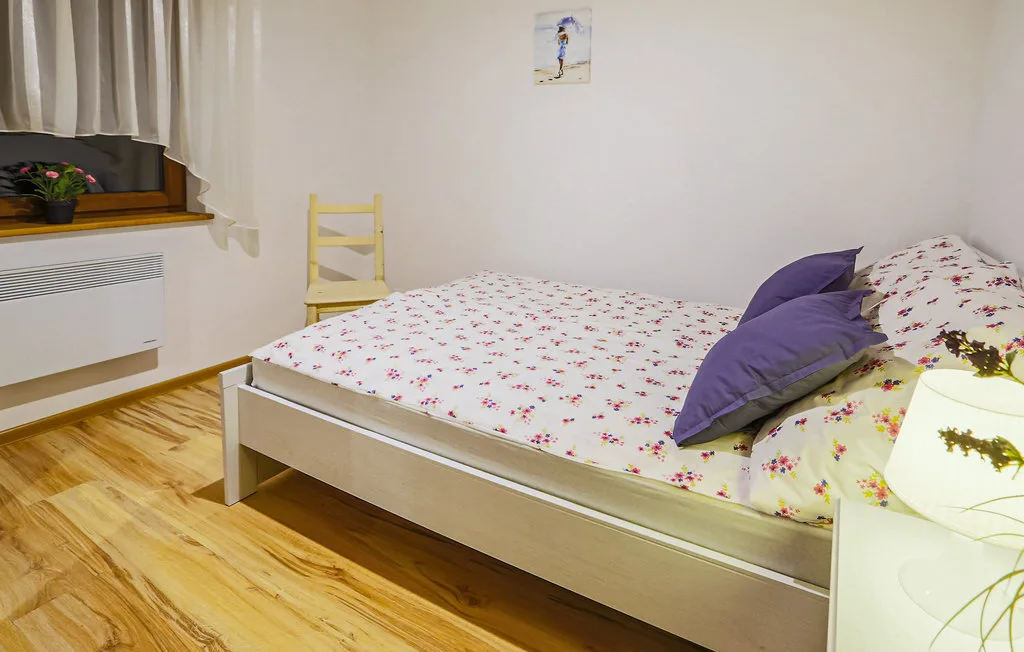 A bedroom with floral bedding and purple pillows beside a window.
