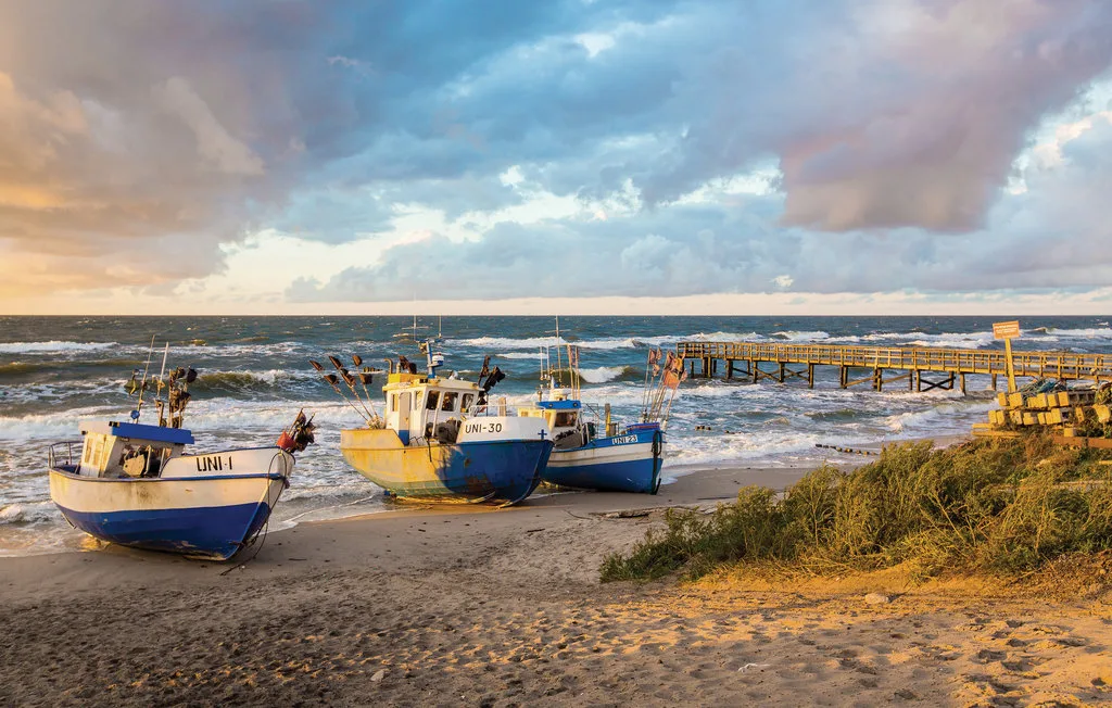 Fishing boats sit on a sandy beach beside a wooden pier.