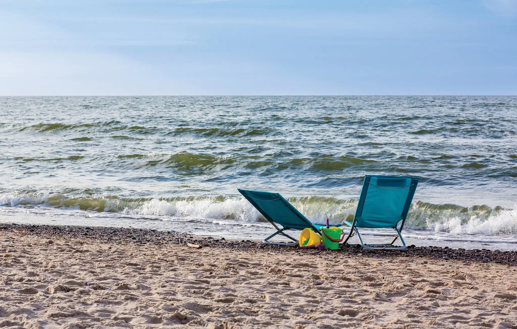 A sandy beach with two folding chairs beside the waves.