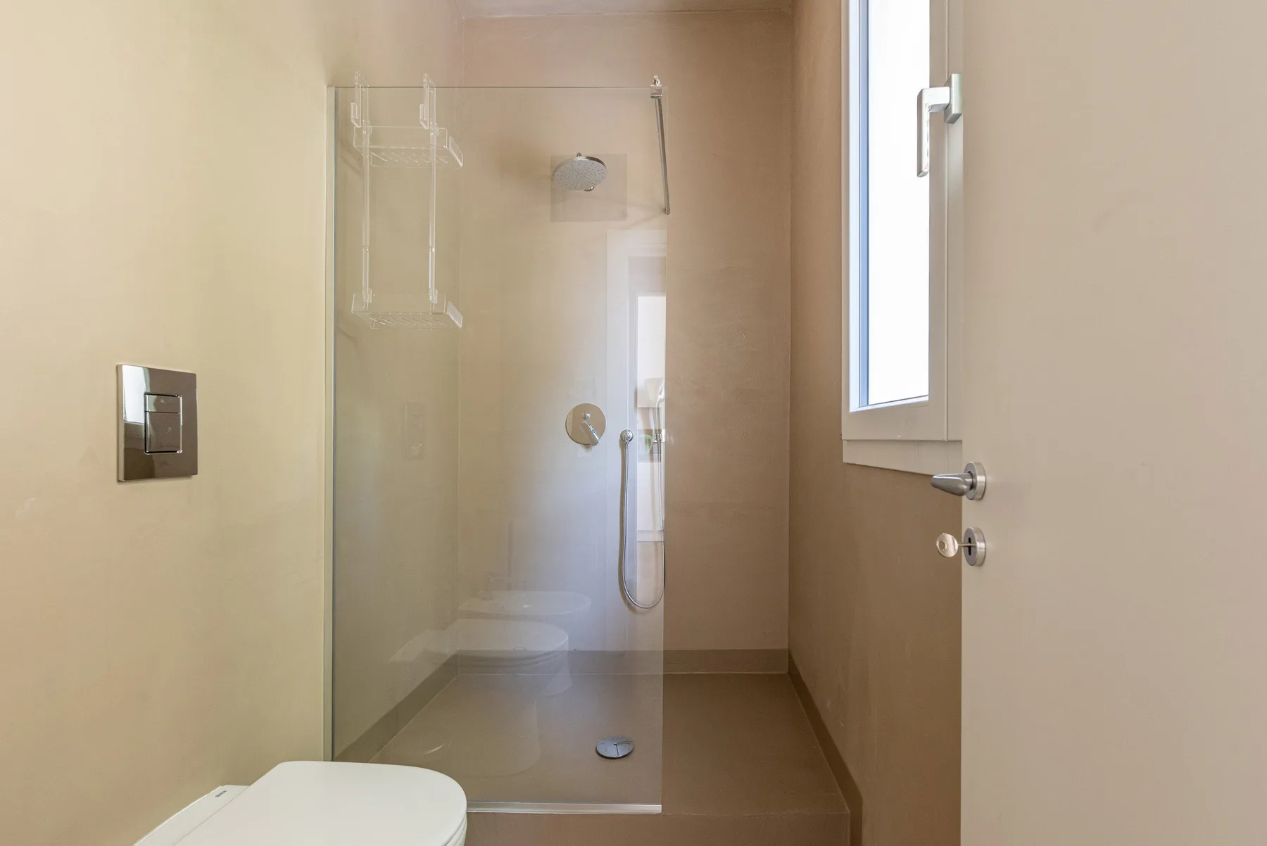 Un baño con una ducha de vidrio y una ventana.