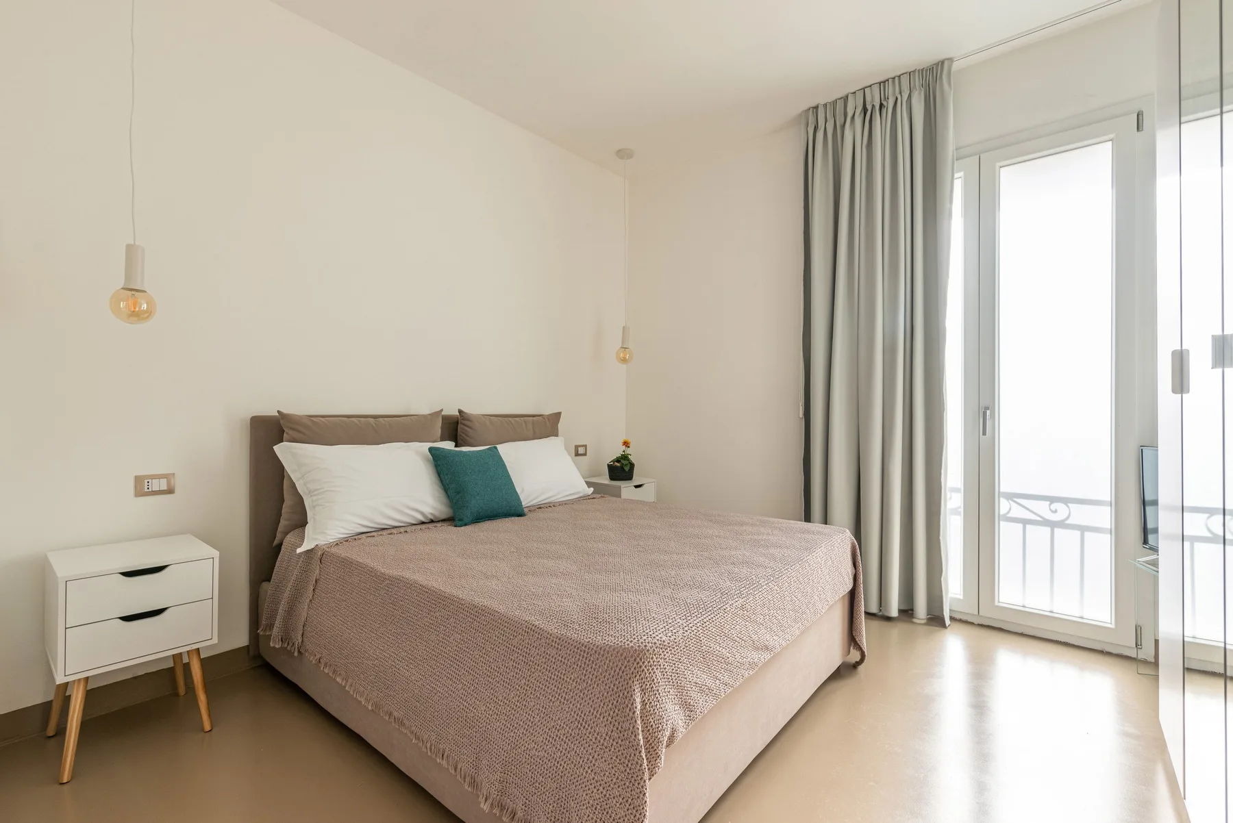 Un dormitorio luminoso con una cama grande y puertas de vidrio que dan a un balcón.