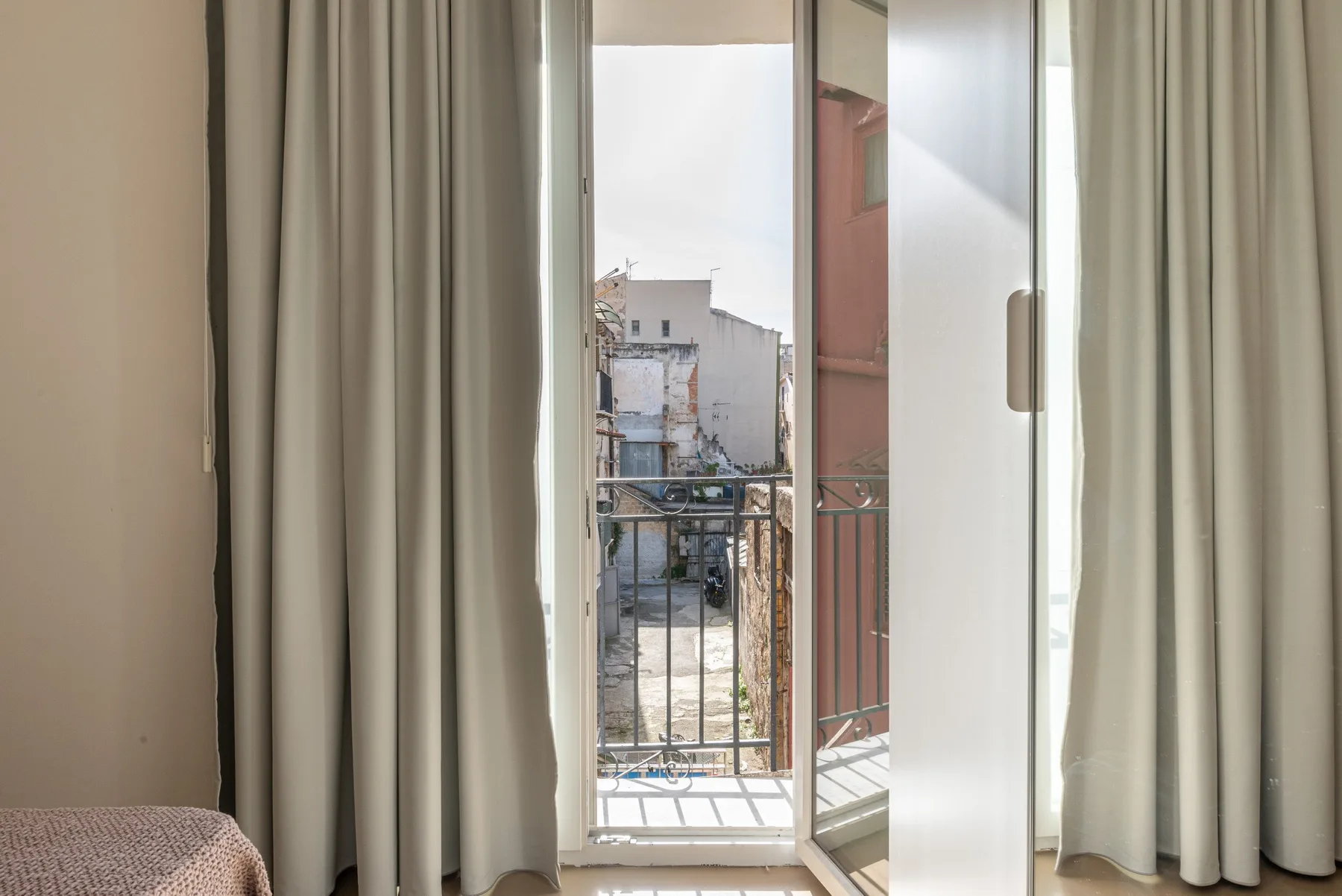 Las cortinas enmarcan una puerta de cristal abierta que da a un pequeño balcón.