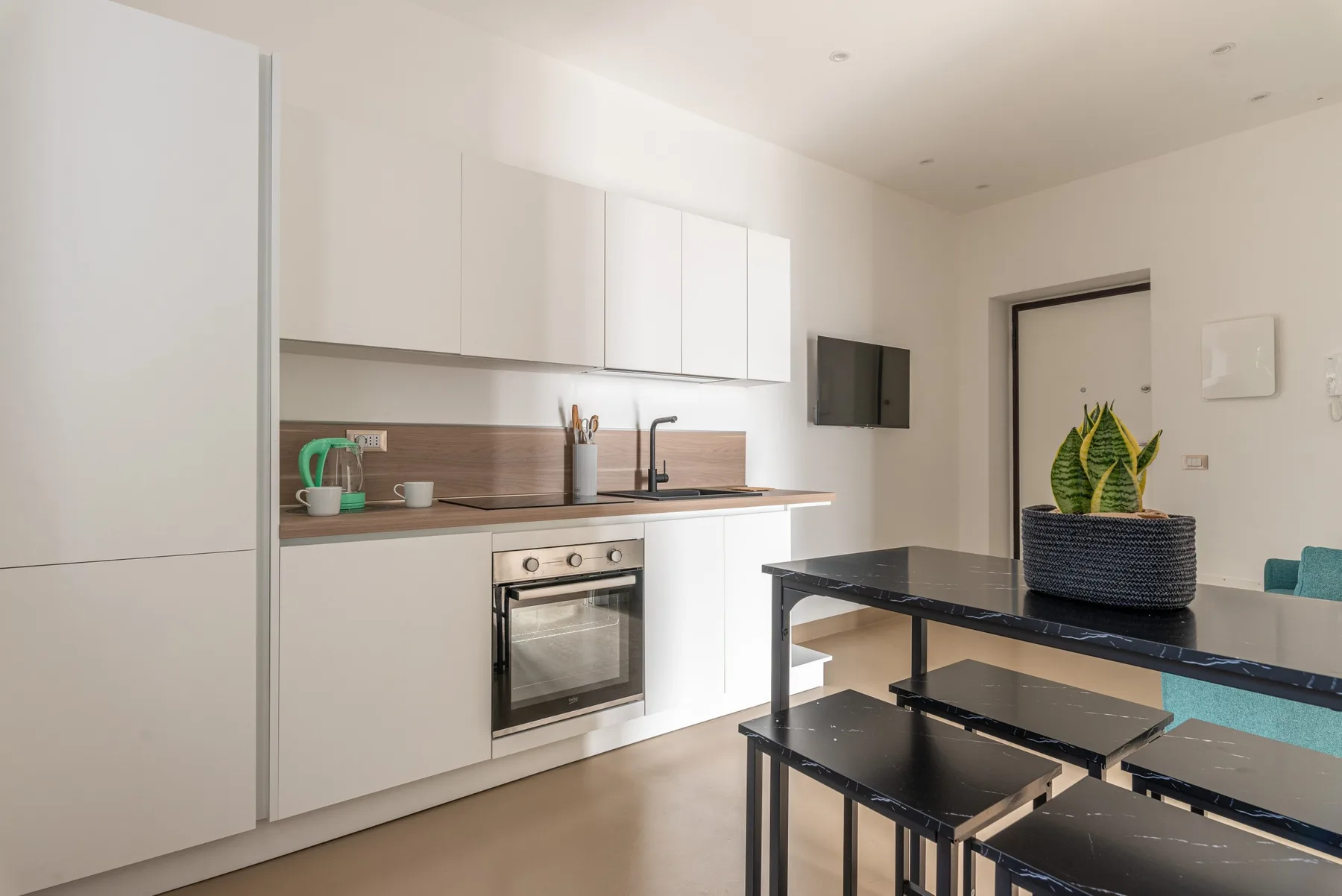 Una cocina moderna y luminosa con gabinetes blancos, horno empotrado y mesa negra.