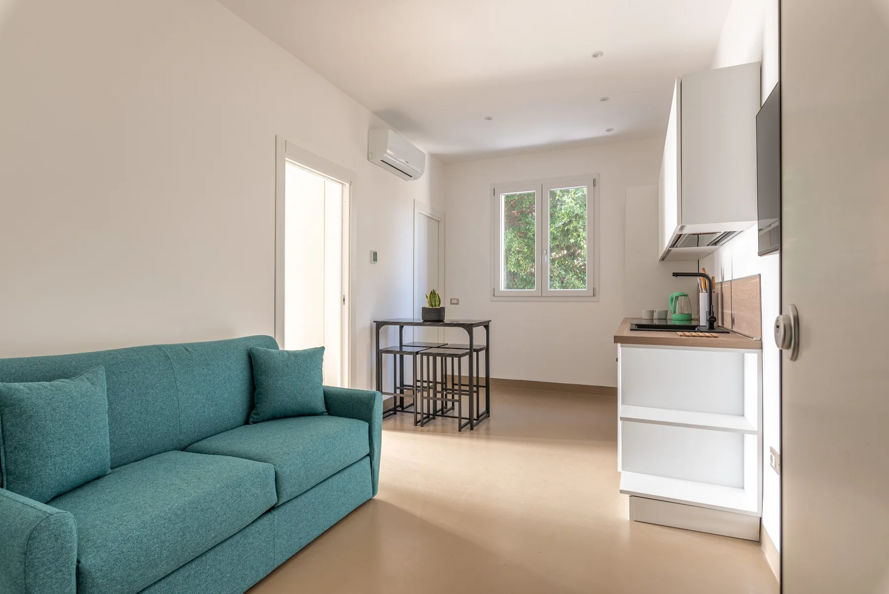 Una sala luminosa con asientos color turquesa y una cocina compacta.