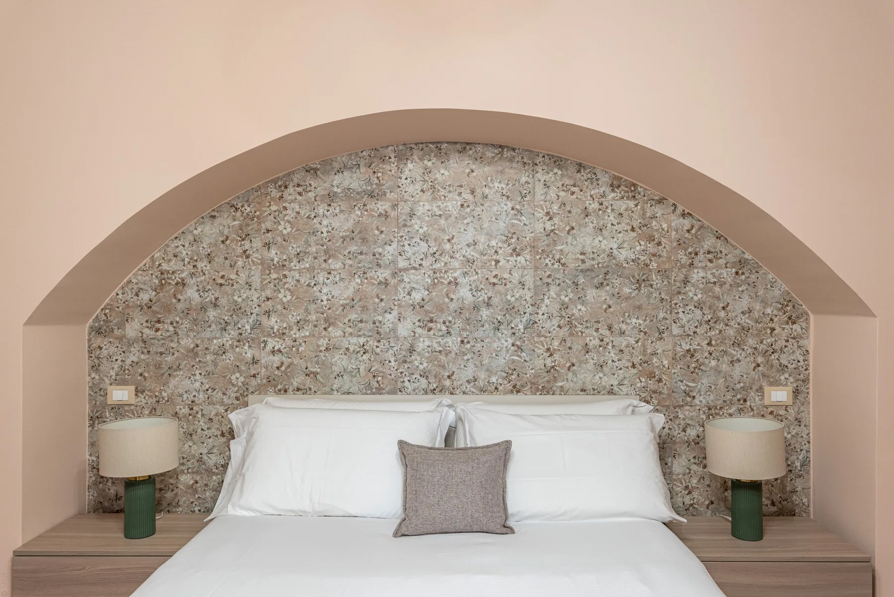 A bed is set against a textured wall beneath a broad arched alcove.