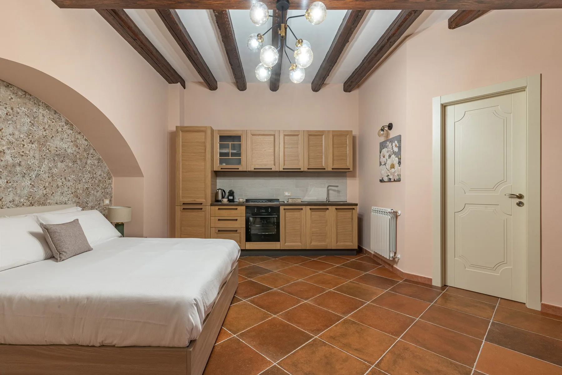 A bedroom with a bed and a small kitchen along the back wall.