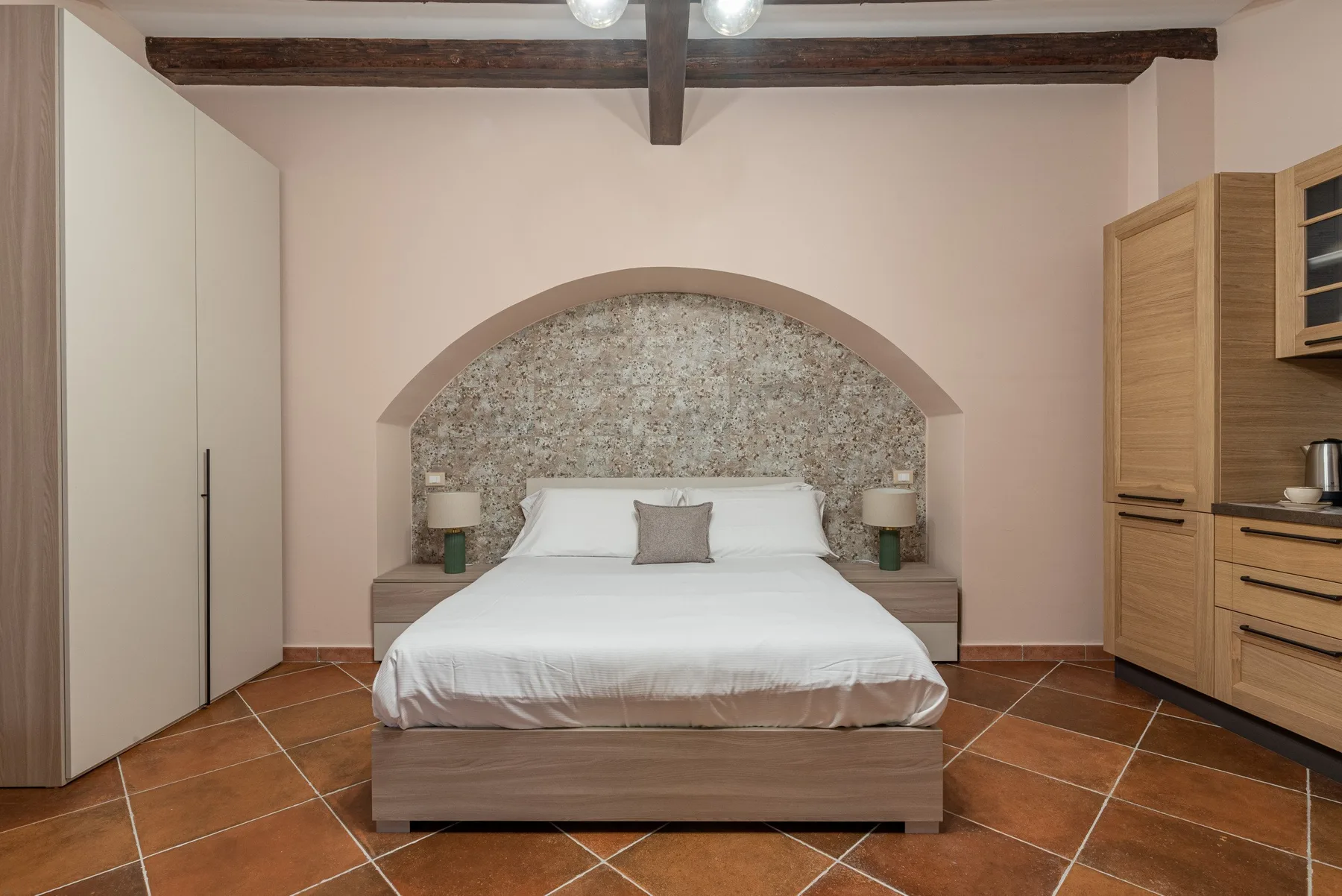 A bedroom with a double bed beneath an arched feature wall.