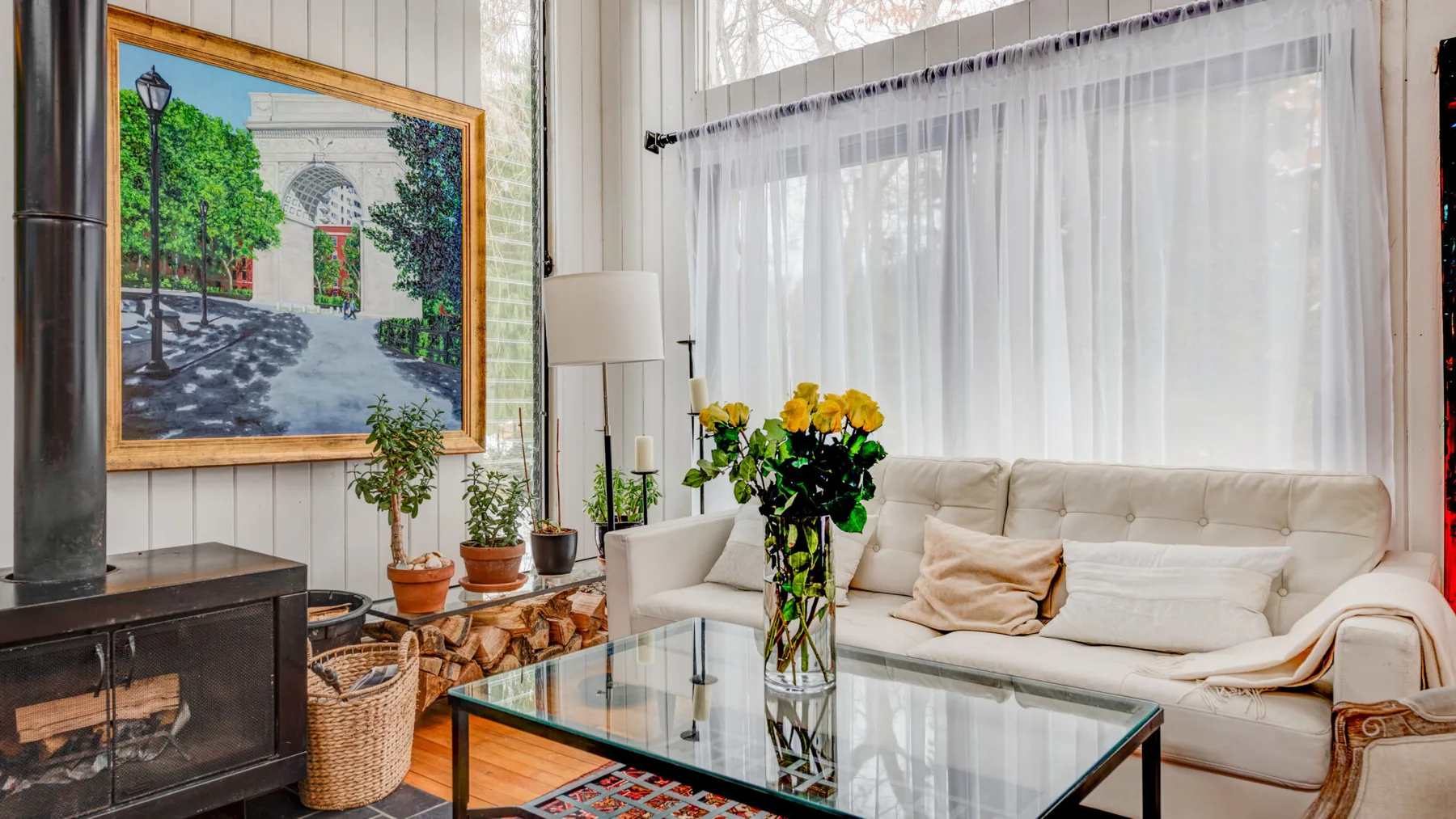 Una sala luminosa con asientos color crema, una mesa de centro de vidrio y una gran ventana con cortinas.