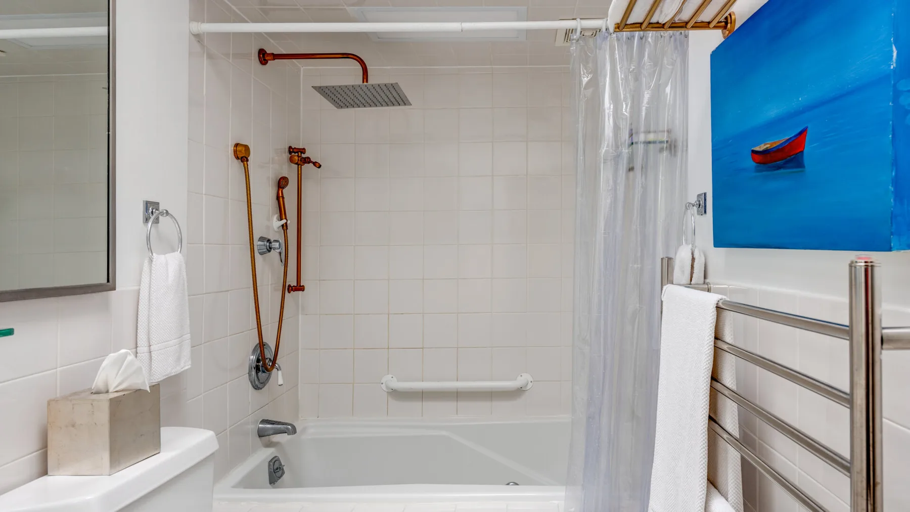 Un baño alicatado con bañera, grifería de ducha y un cuadro azul del océano.