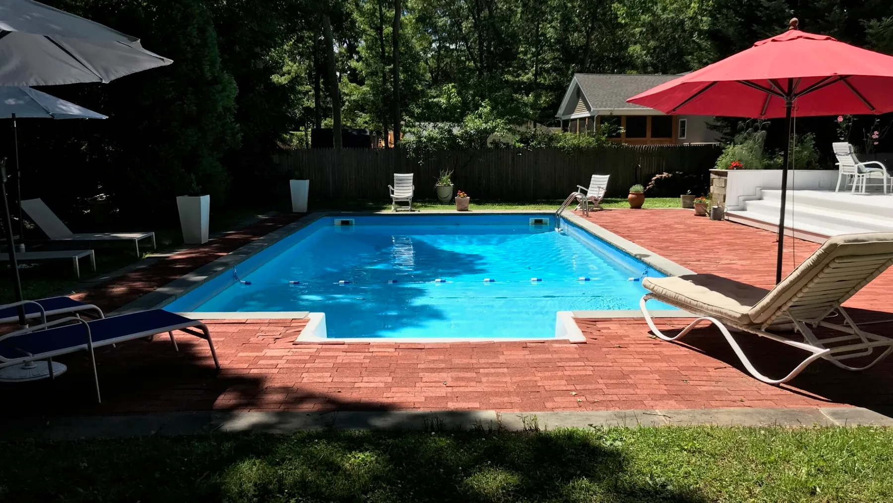 Una piscina al aire libre está rodeada por un patio de ladrillo y sillas reclinables.