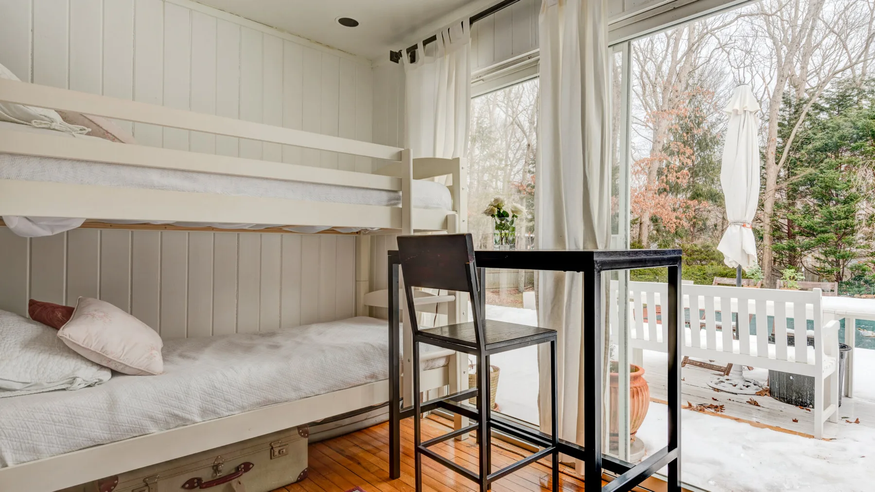 Una habitación luminosa con literas, una mesa y grandes ventanas con vistas a un balcón.