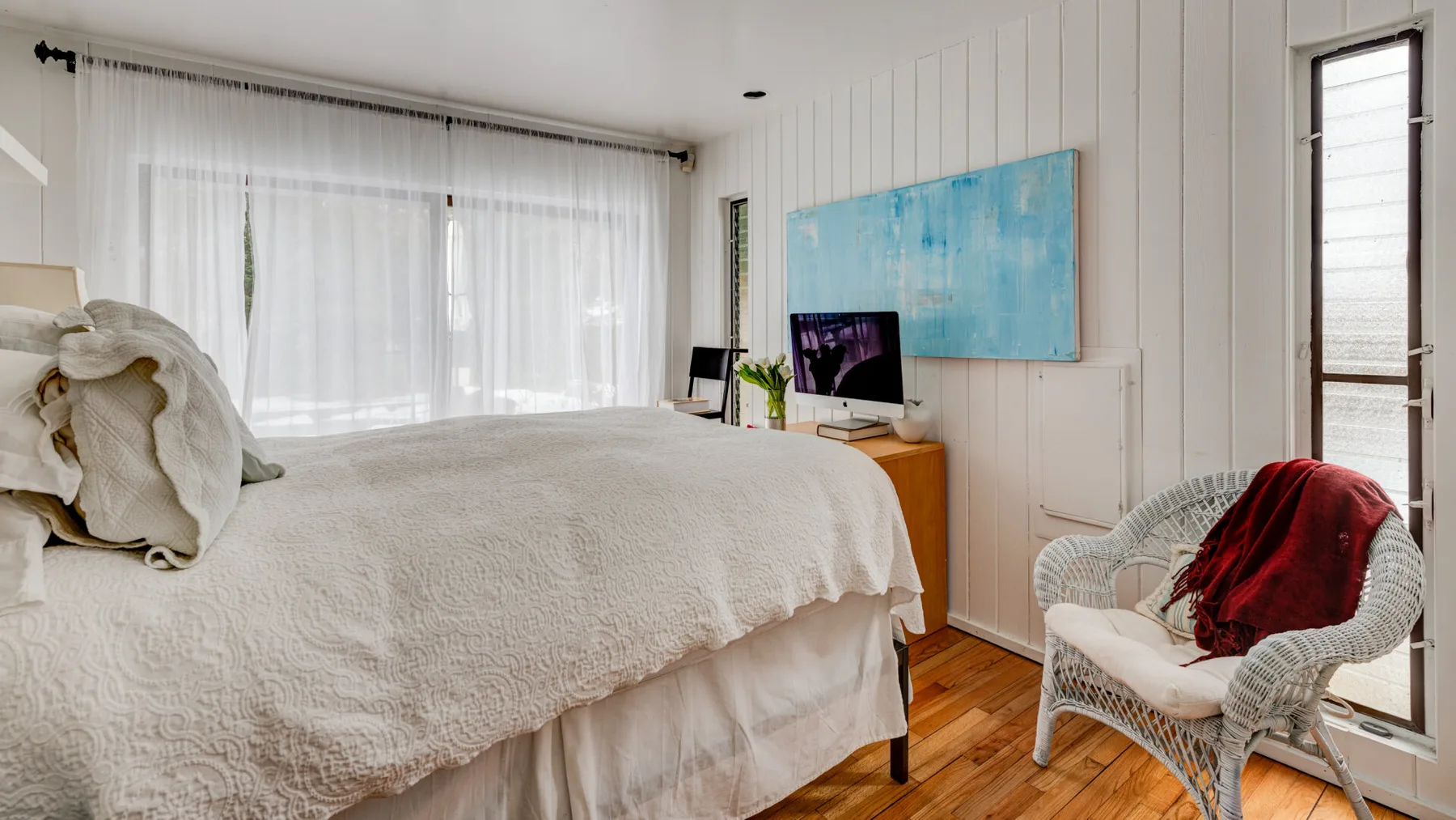 Un dormitorio luminoso con una cama tendida y una silla de mimbre junto a la ventana.