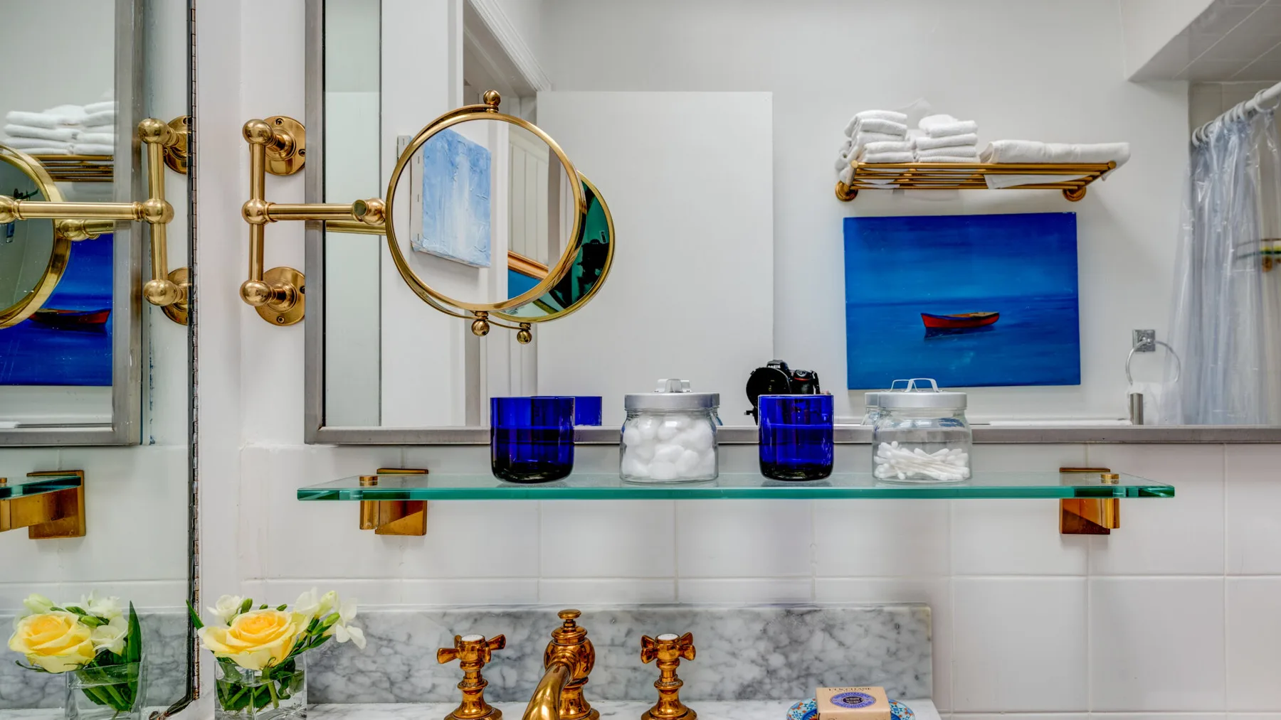Un lavabo de baño con espejo, estante de vidrio y una obra azul.