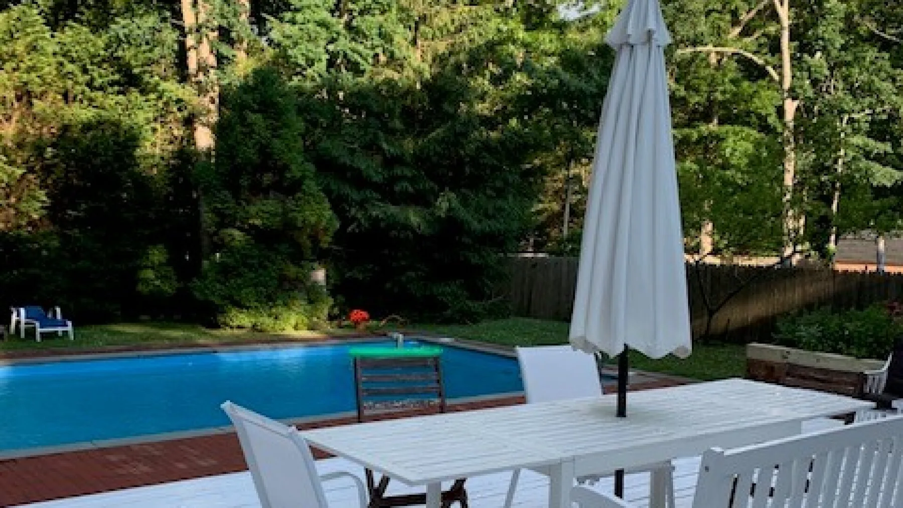 Una piscina exterior junto a una mesa de patio y una sombrilla cerrada.