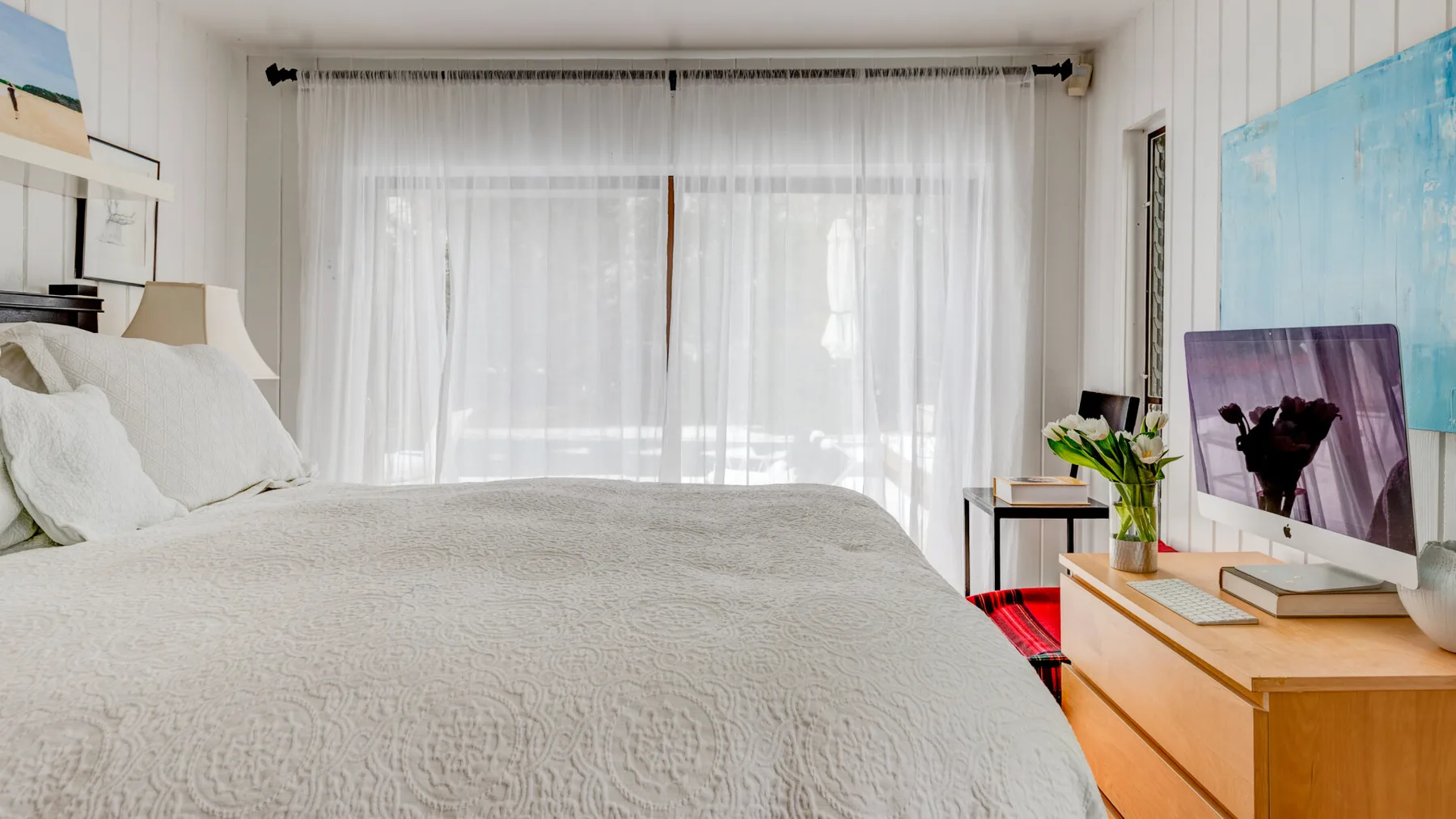 Un dormitorio luminoso con una cama grande y cortinas translúcidas frente a la ventana.