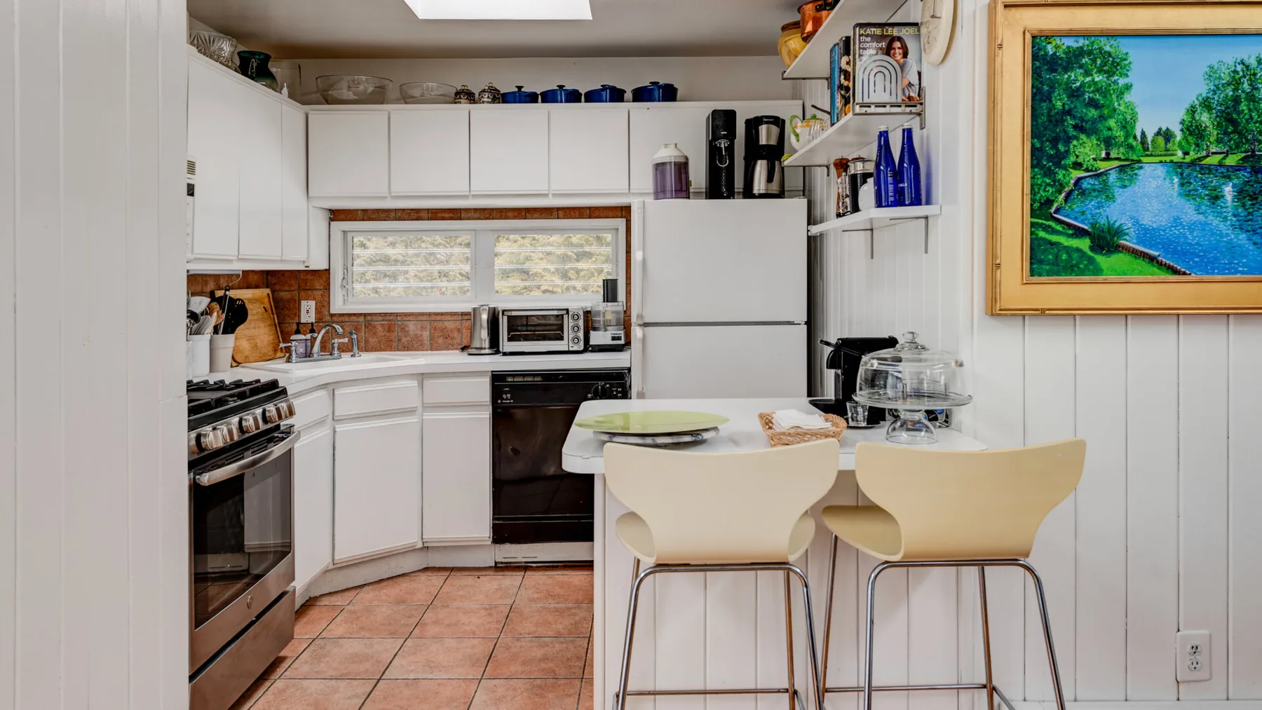 Una cocina luminosa con gabinetes blancos, electrodomésticos y una pequeña barra para comer.