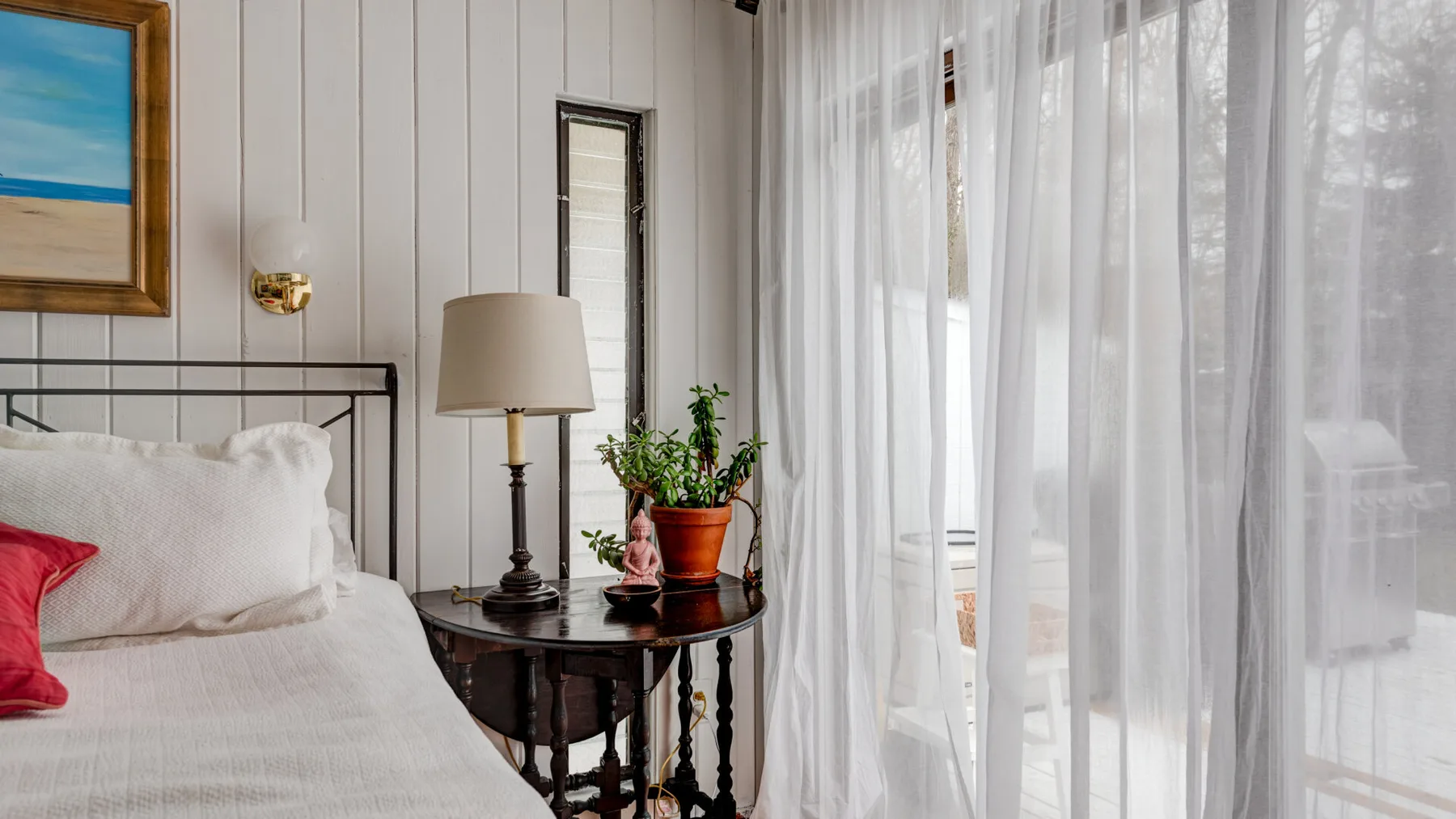 Un dormitorio con una cama junto a una mesa pequeña y cortinas translúcidas.