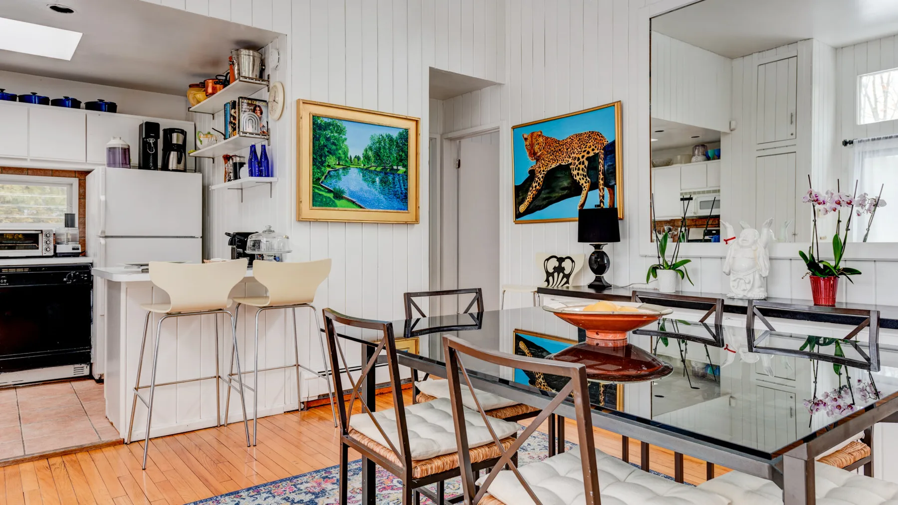 Una cocina luminosa con zona de comedor, mesa de vidrio y cuadros.