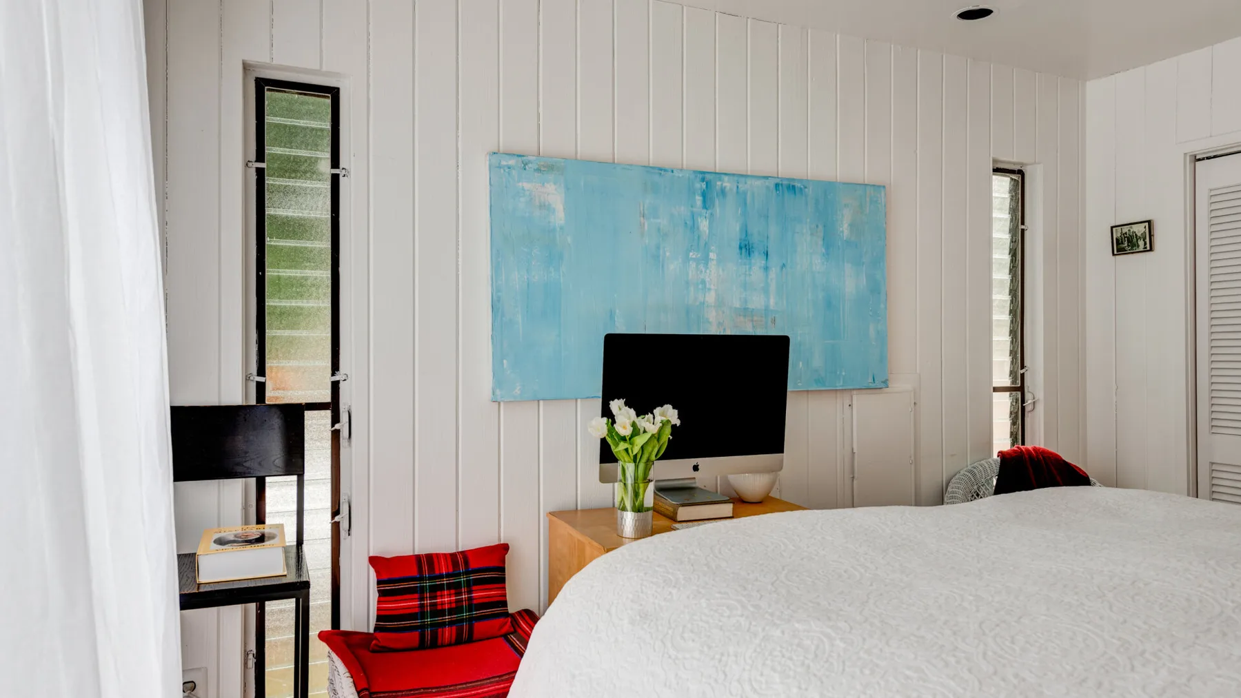 Un dormitorio con una cama, un televisor y una obra azul en la pared.