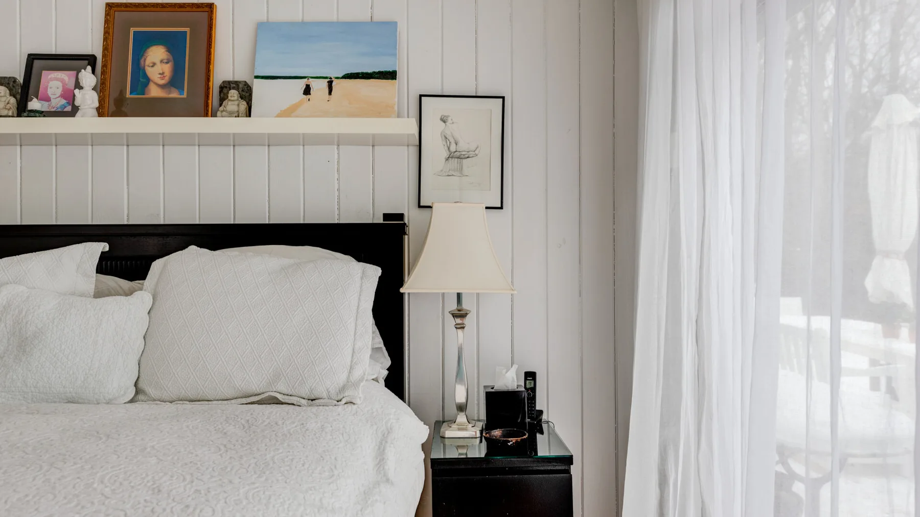 Un dormitorio con una cama tendida junto a una ventana con cortinas translúcidas.