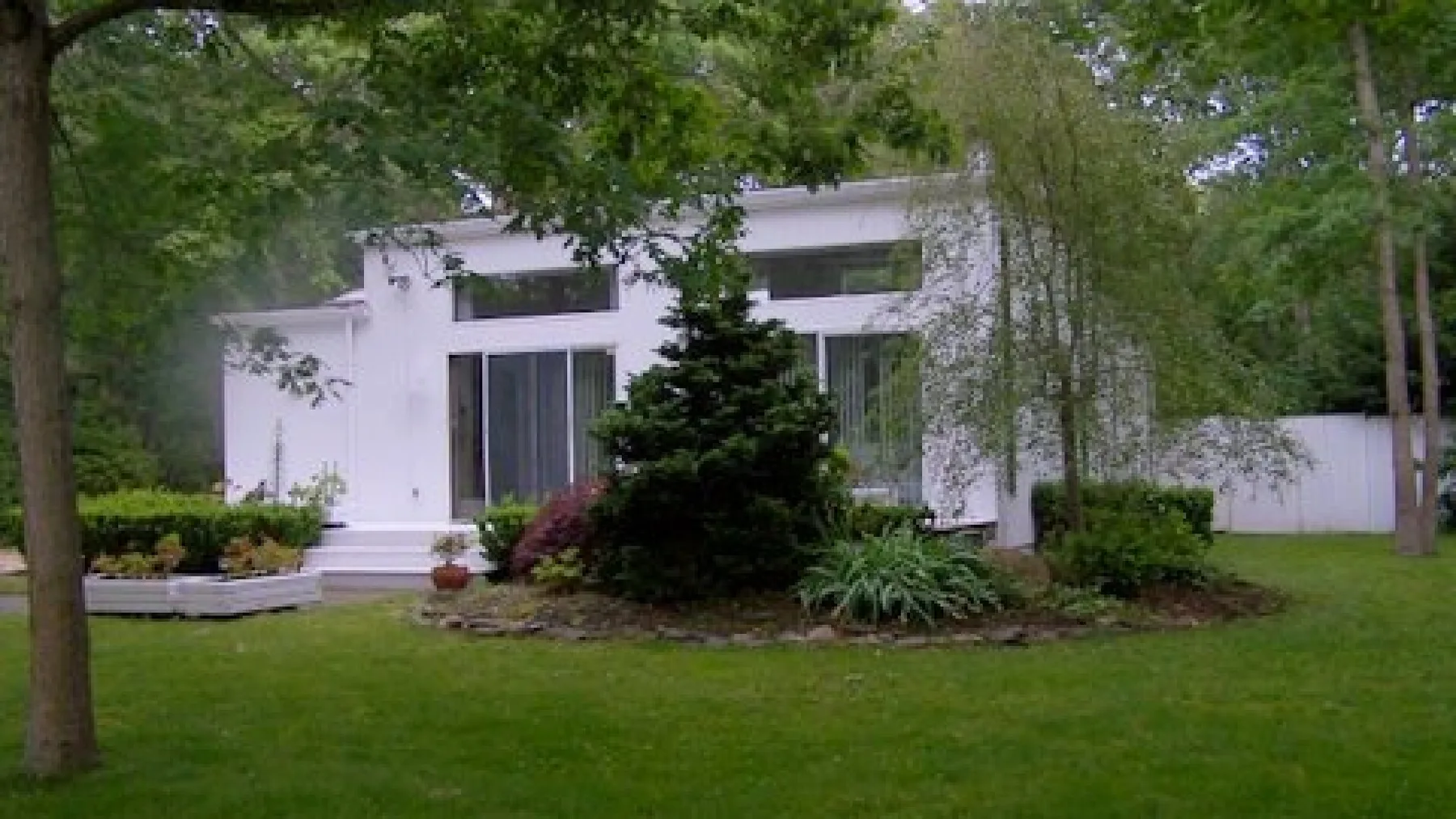 Una casa blanca se encuentra detrás de un césped verde y un jardín ajardinado.