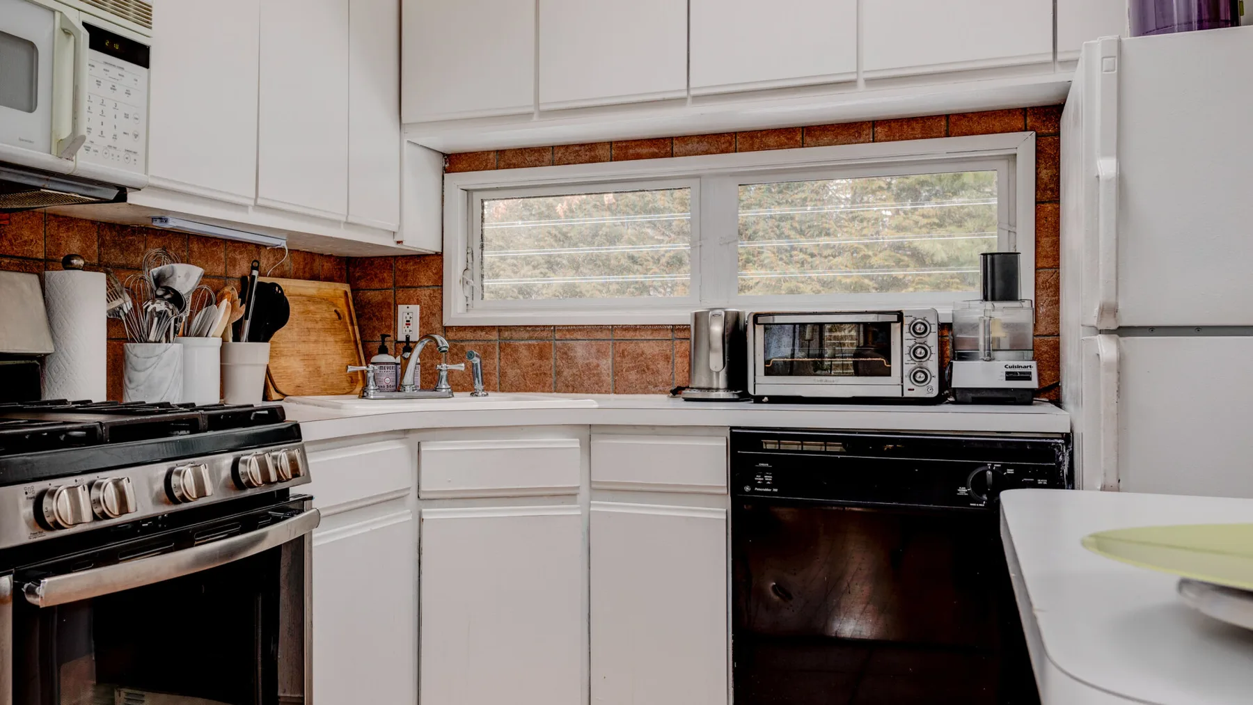 Una cocina luminosa con gabinetes blancos, una ventana y electrodomésticos sobre la encimera.