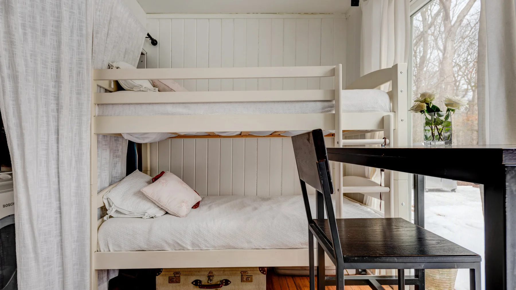 Un dormitorio luminoso con literas, un escritorio y una ventana grande.