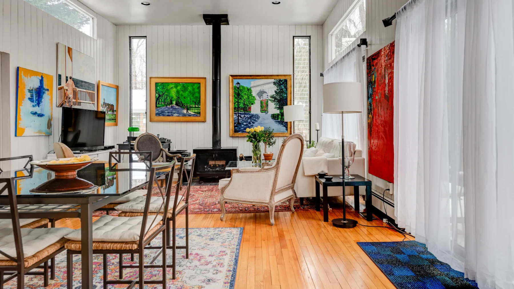 Una sala luminosa con asientos, una chimenea y obras de arte coloridas.