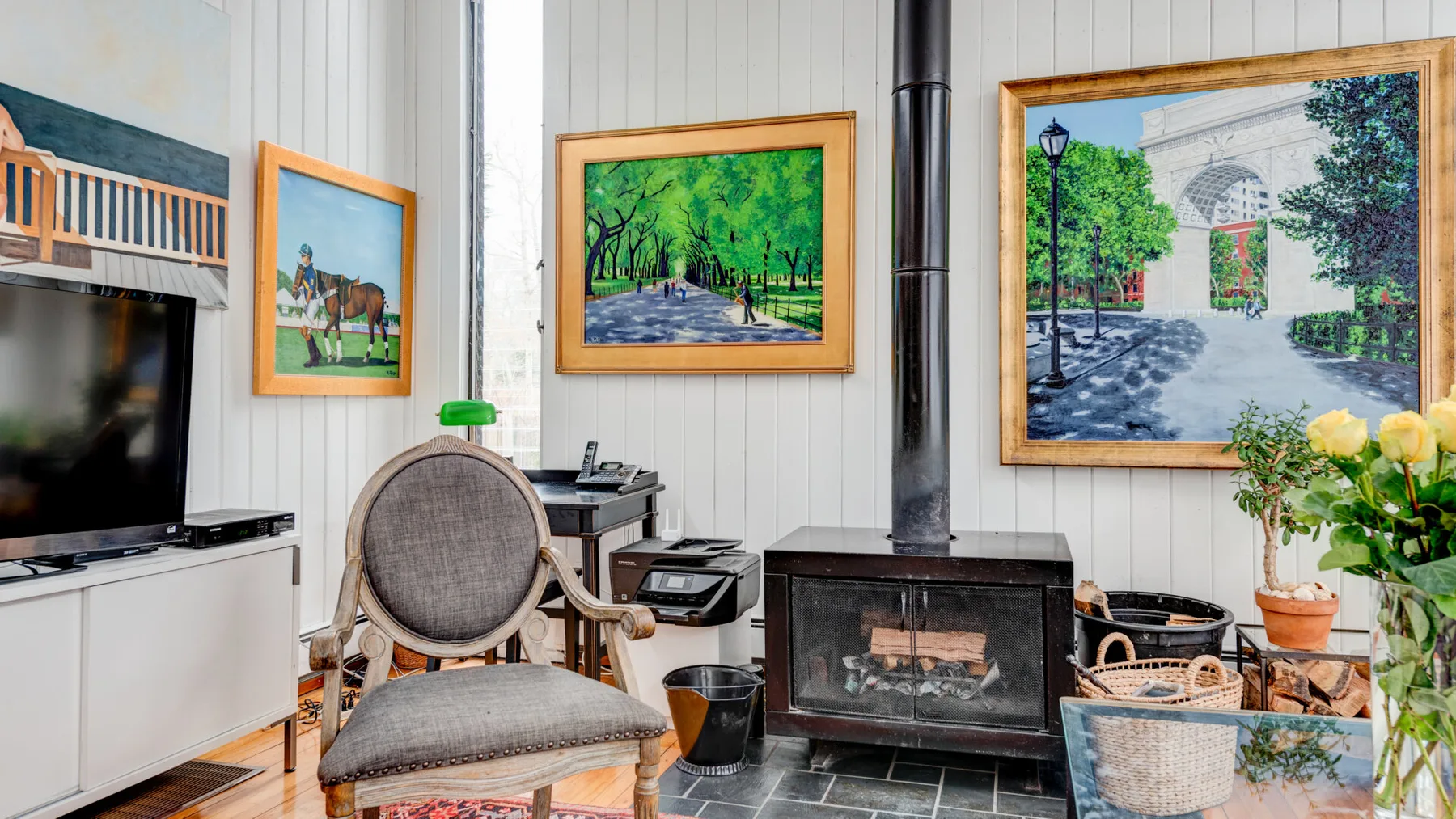 Una sala de estar con chimenea, televisor y cuadros de paisajes enmarcados.