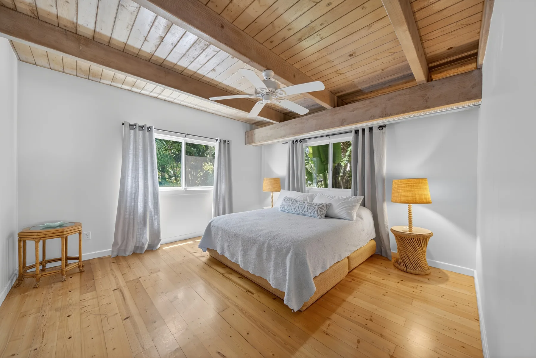 Un dormitorio luminoso con una cama grande, suelo de madera y techo alto de madera.
