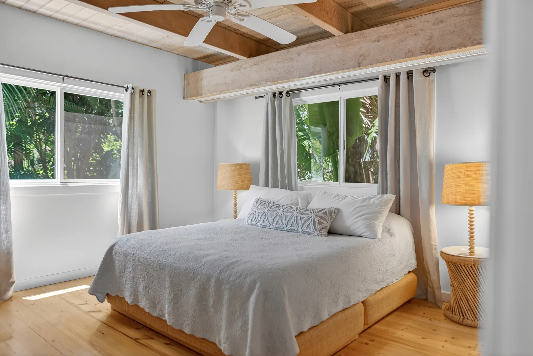 Un dormitorio con una cama entre ventanas con vistas a la vegetación.